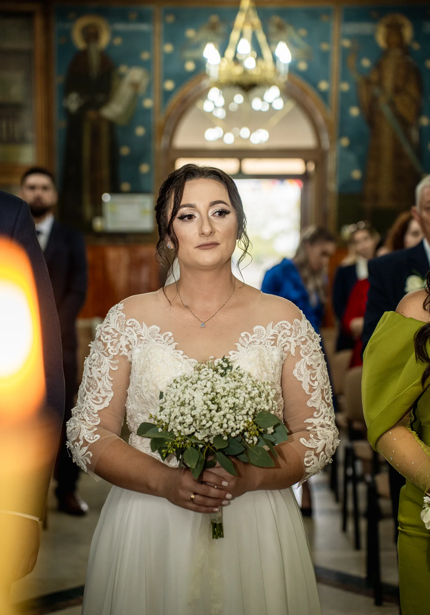 Mireasa cu buchet alb în biserică, în timpul slujbei, cu frescă și candelabru în fundal