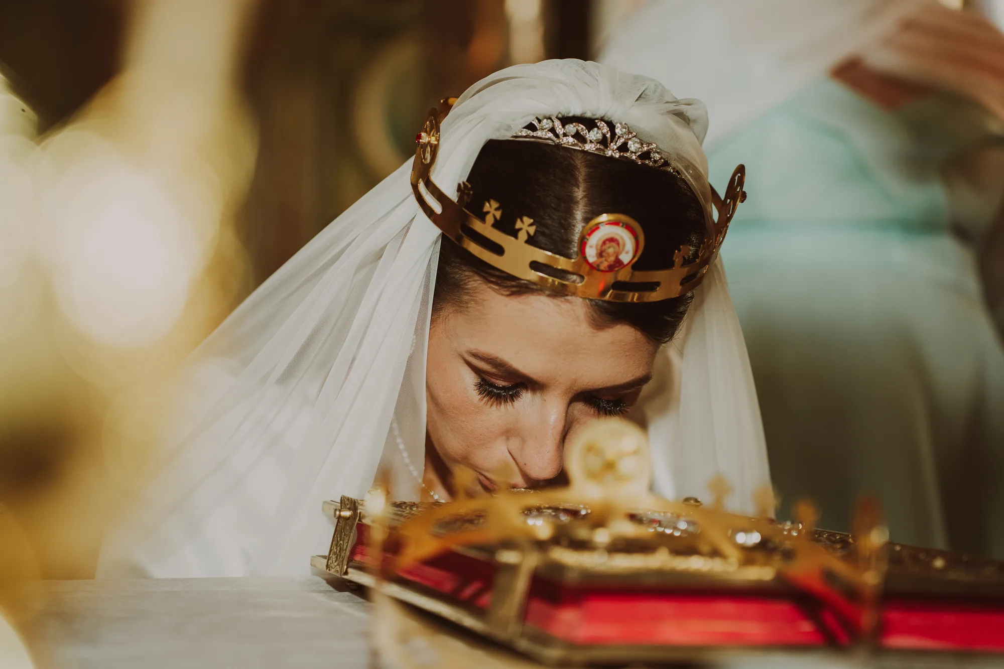 Mireasa, cu cununia de metal aurit peste voal, se apleacă să sărute Evanghelia de pe masa din mijlocul bisericii