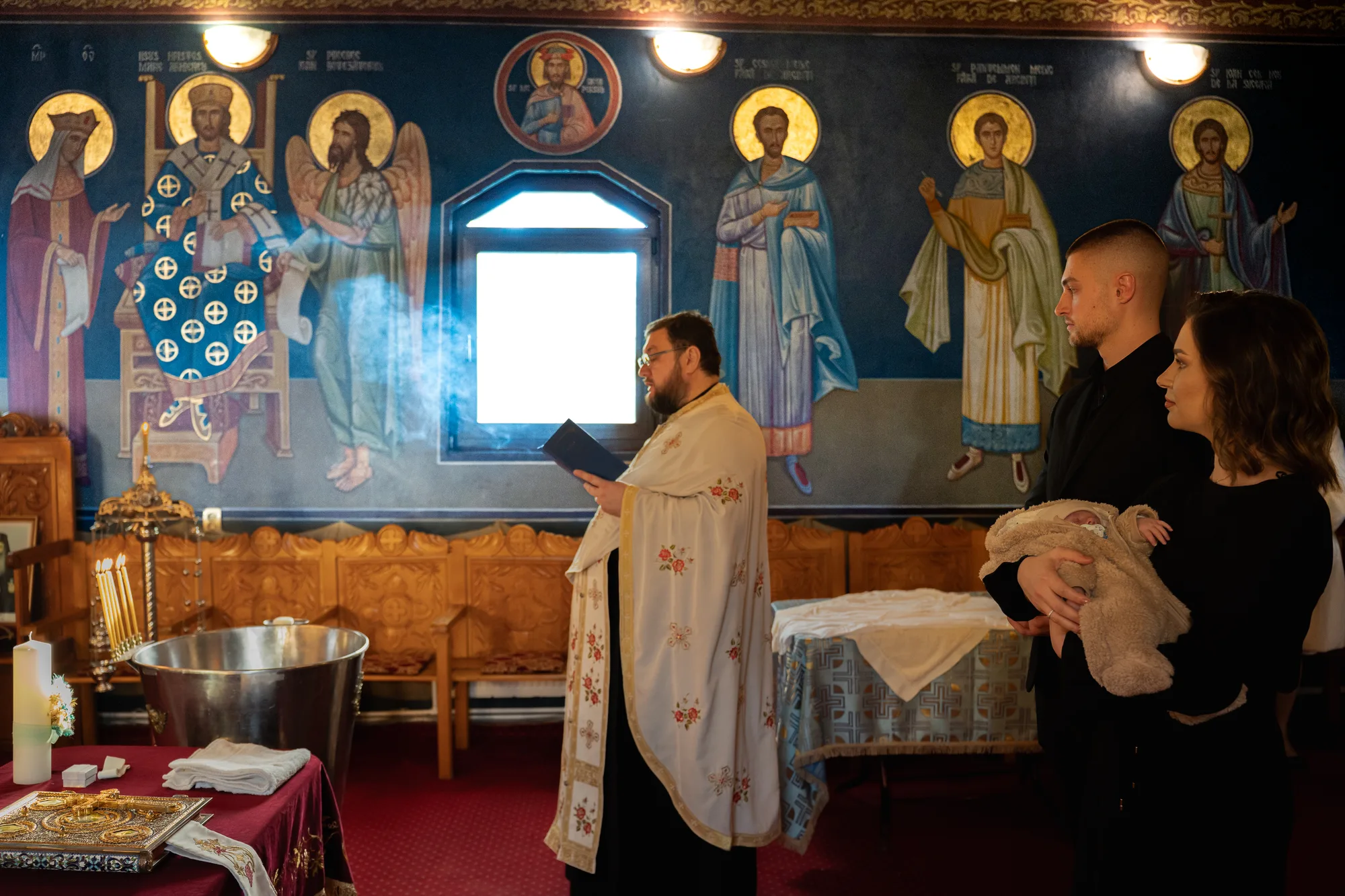 Slujba de botez în biserica pictată: preotul cu cădelnița, în fumul de tămâie